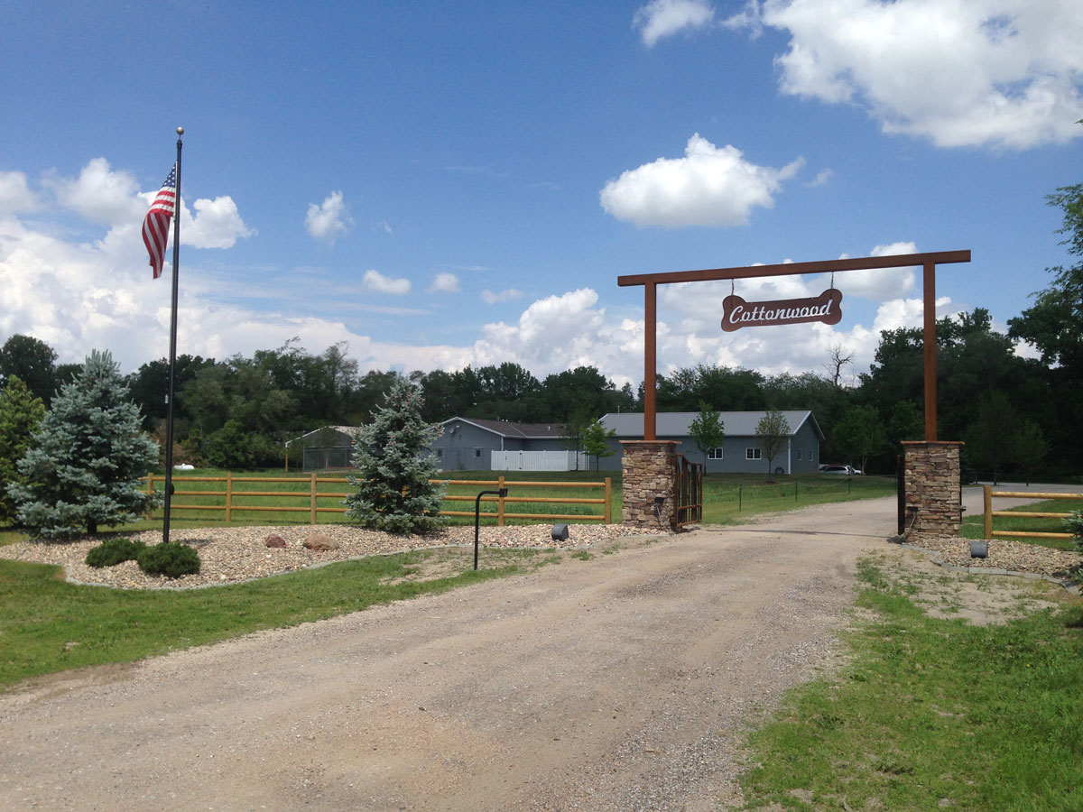 The Cottonwood Pet Resort entrance gate with its hanging sign, under a blue summer sky