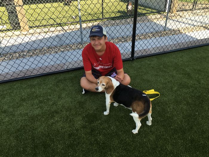 A Cottonwood staff member sitting on the turf with a happy beagle